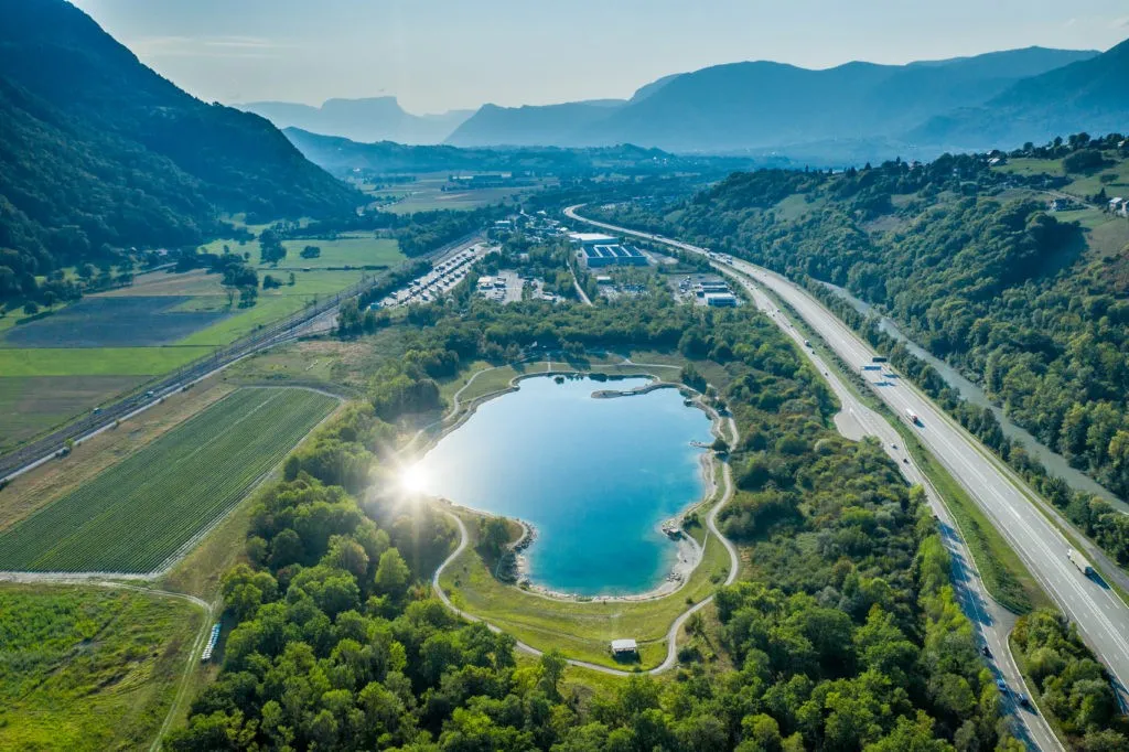 Vue aérienne d'une vallée alpine : plan d'eau, autoroute, voie ferrée, terres agricoles et zone d'activités en fond de vallée